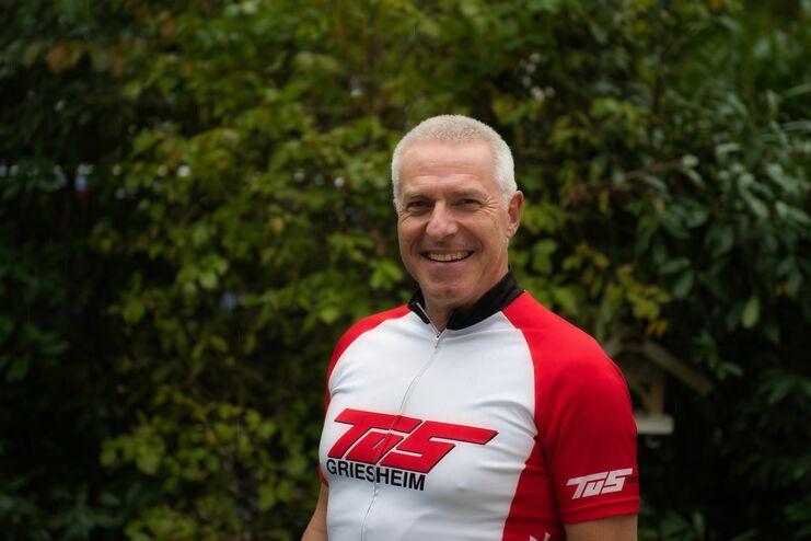 Lächelnder Mann in einem bunte Radtrikot vor grünem Hintergrund.