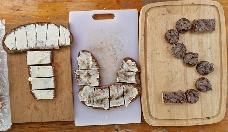Drei unterschiedlich belegte Brotscheiben liegen auf Holz- und Plastikunterlagen, eine mit Frischkäse, eine mit Aufstrich.