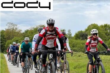 Gruppe von Radfahrern in Rot und Schwarz fährt auf einem Fahrradweg, umgeben von grüner Landschaft.