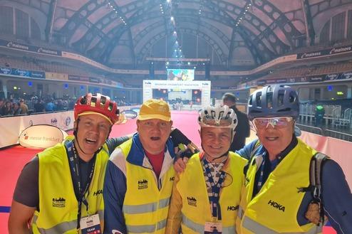 Vier Personen in Sicherheitswesten und Helmen posieren lächelnd in einer Veranstaltungshalle während des Frankfurt Marathons.