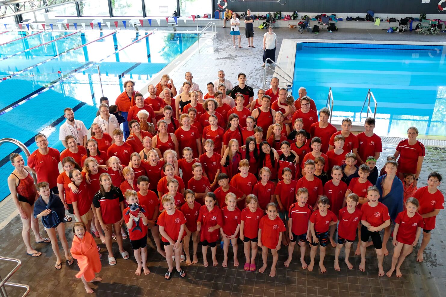 Gruppenshot von Schwimmern in roten Shirts am Schwimmbecken, lächelnd und posierend für das Foto.