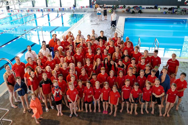 Gruppenshot von Schwimmern in roten Shirts am Schwimmbecken, lächelnd und posierend für das Foto.