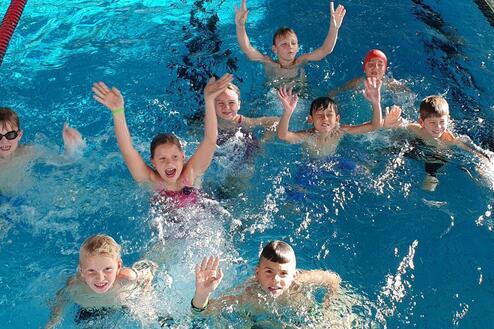 Gruppe von Kindern im Wasser, die fröhlich winken und Spaß im Schwimmbad haben.