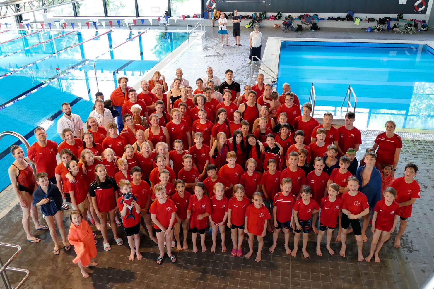 Gruppenshot von Schwimmern in roten Shirts am Schwimmbecken, lächelnd und posierend für das Foto.