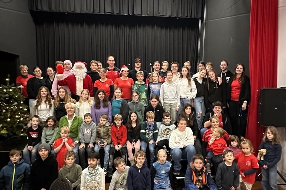 Gruppenfoto von Kindern und Jugendlichen mit Weihnachtsmann vor einer festlich dekorierten Bühne.