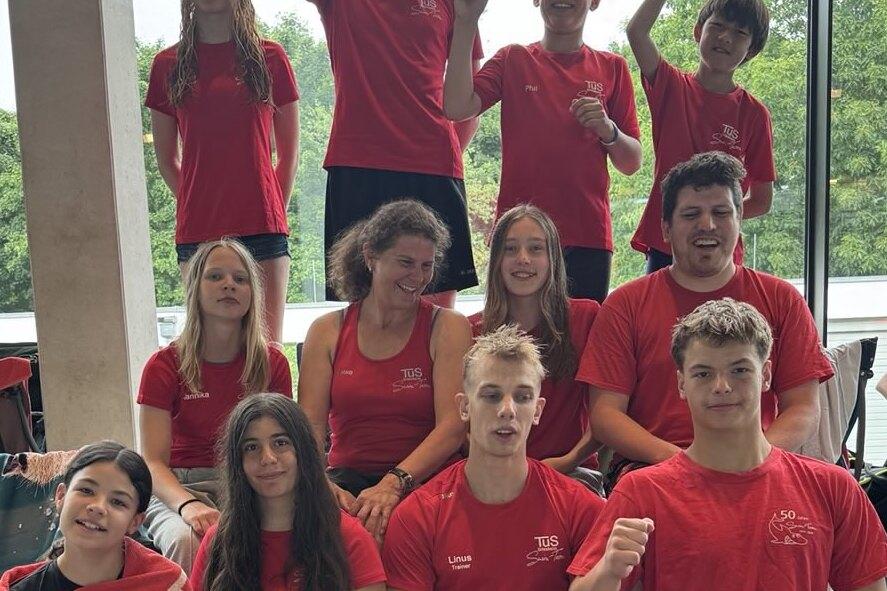 Gruppe von Schwimmern in roten T-Shirts posiert fröhlich vor einem Fenster im Schwimmbad.