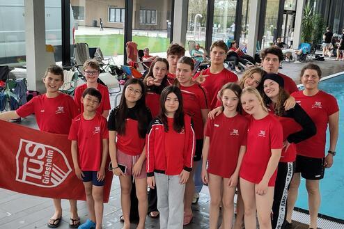 Gruppe junger Schwimmer in roten T-Shirts mit Vereinslogo TUS Griesheim, lächeln am Schwimmbeckenrand.