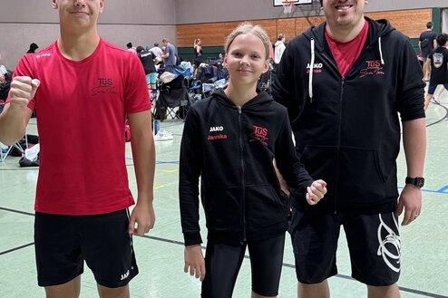 Drei Personen in Sportbekleidung stehen in einer Sporthalle und posieren für ein Foto.