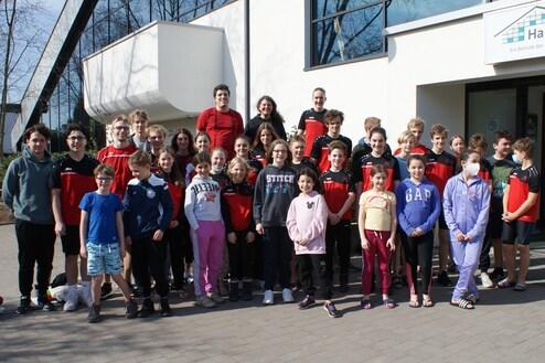 Gruppenfoto mit Kindern und Jugendlichen in Sportkleidung vor einem modernen Gebäude an einem sonnigen Tag.