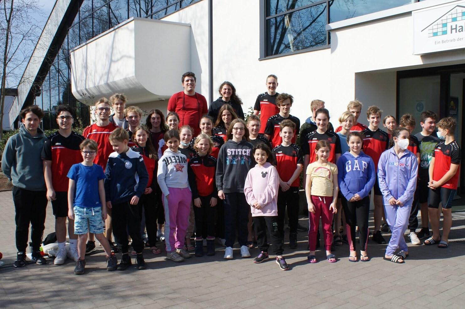Gruppenfoto mit Kindern und Jugendlichen in Sportkleidung vor einem modernen Gebäude an einem sonnigen Tag.