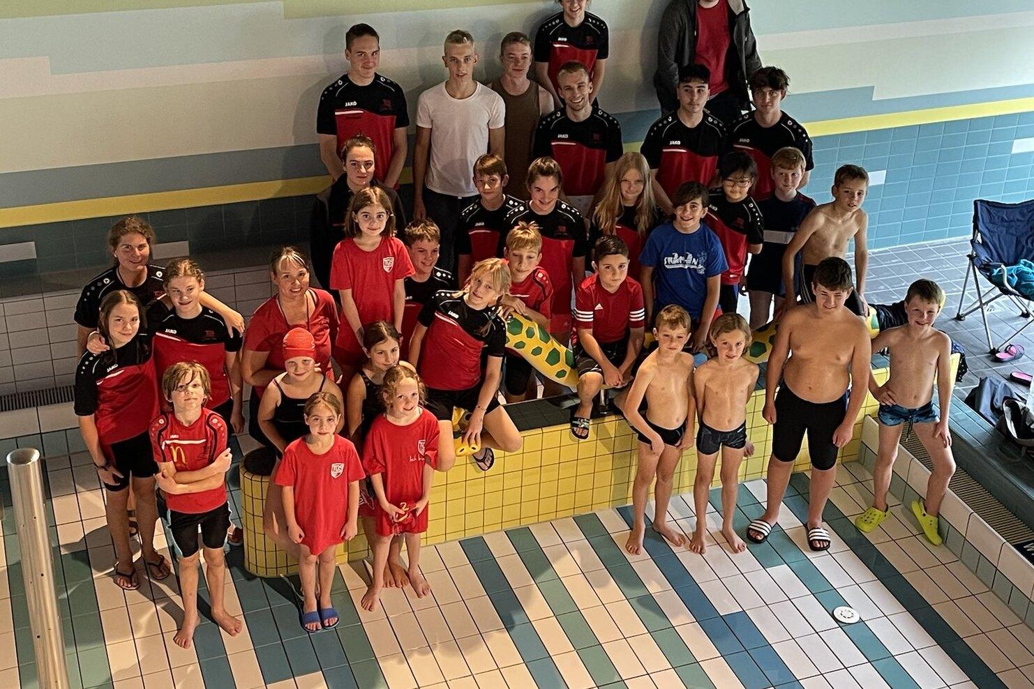 Gruppenshot von Kindern und Jugendlichen in Badebekleidung, die in einem Schwimmbad posieren.