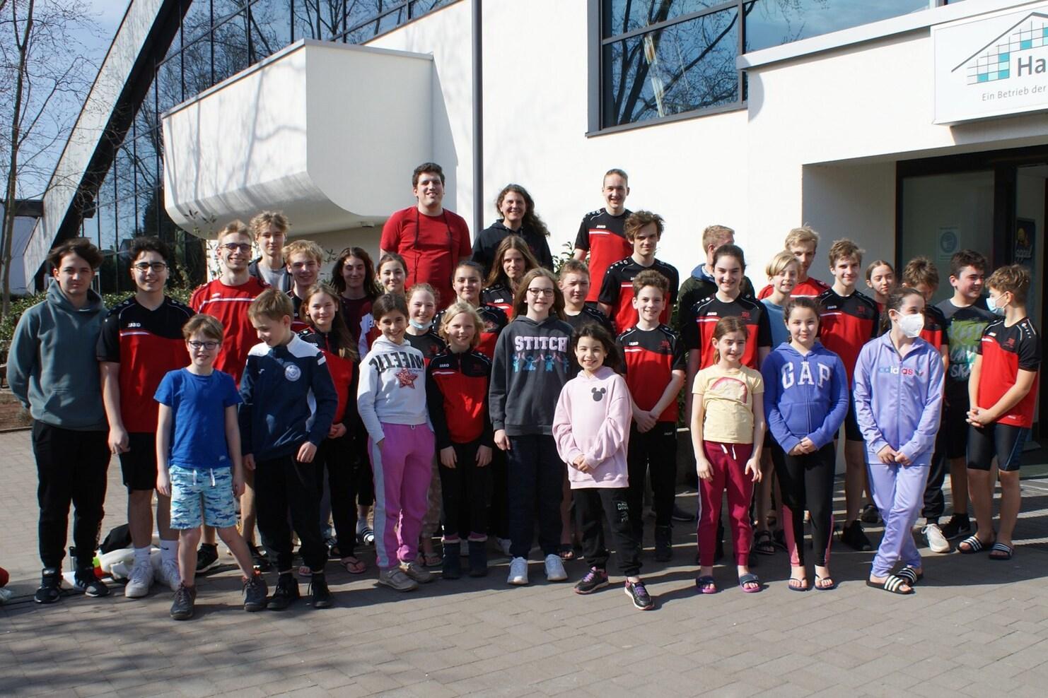 Gruppenfoto mit Kindern und Jugendlichen in Sportkleidung vor einem modernen Gebäude an einem sonnigen Tag.