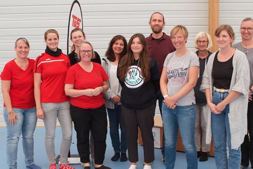 Gruppenfoto von zwölf Personen in Sportkleidung in einer Sporthalle, lächelnd vor einer hellen Wand.