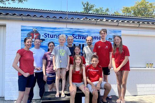 Gruppennaufnahme von Schwimmern auf dem Treppchen nach einem Wettkampf mit Medaillen und einer Banner im Hintergrund.