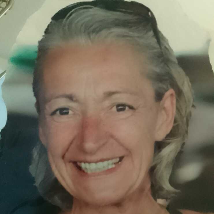 Nahaufnahme eines lächelnden Gesichts einer älteren Frau mit grauen Haaren und einem Tanktop.