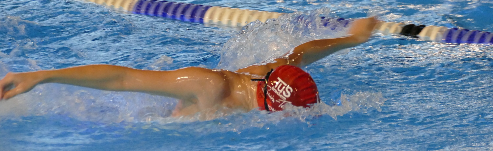 Schwimmer f&uuml;hrt einen Schmetterlingsschwimmzug in einem Becken mit blauer Wasseroberfl&auml;che und Markierungsleinen aus.
