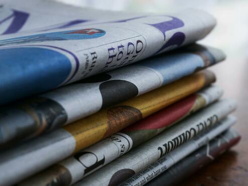 Nahaufnahme eines gestapelten Zeitungsbündels mit unterschiedlichen Titelseiten und Farben.