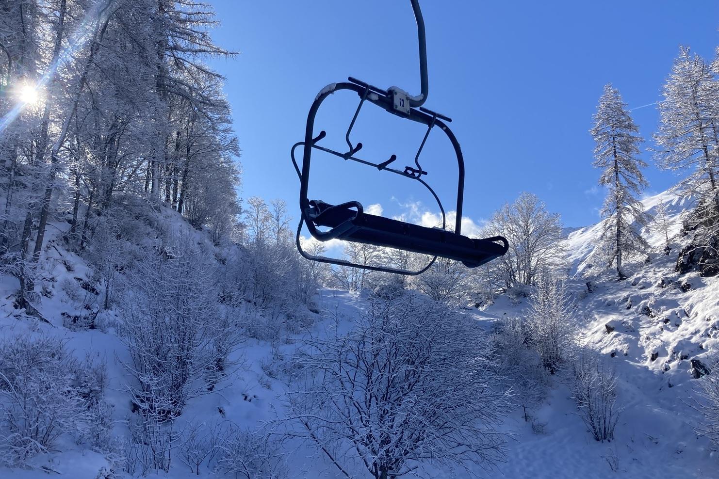 Schwebelift in winterlicher Landschaft mit schneebedeckten Bäumen und klarem, blauem Himmel im Hintergrund.