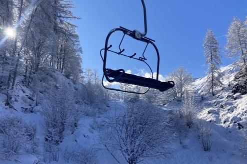 Schwebelift in winterlicher Landschaft mit schneebedeckten Bäumen und klarem, blauem Himmel im Hintergrund.