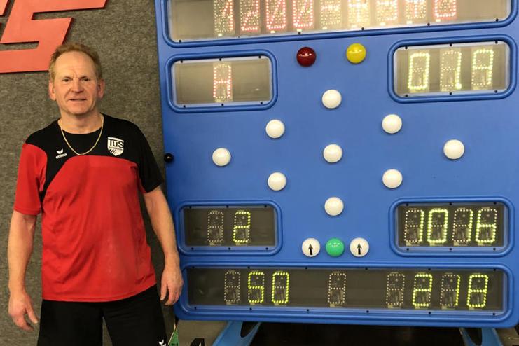 Mann in Sportkleidung steht neben einer digitalen Anzeigetafel mit Spielständen auf einem Tischtennisplatz.