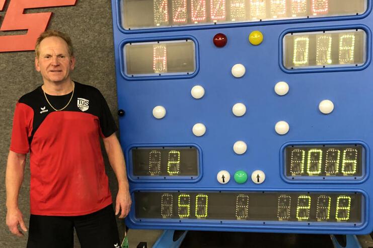 Mann in Sportkleidung steht neben einer digitalen Anzeigetafel mit Spielständen auf einem Tischtennisplatz.