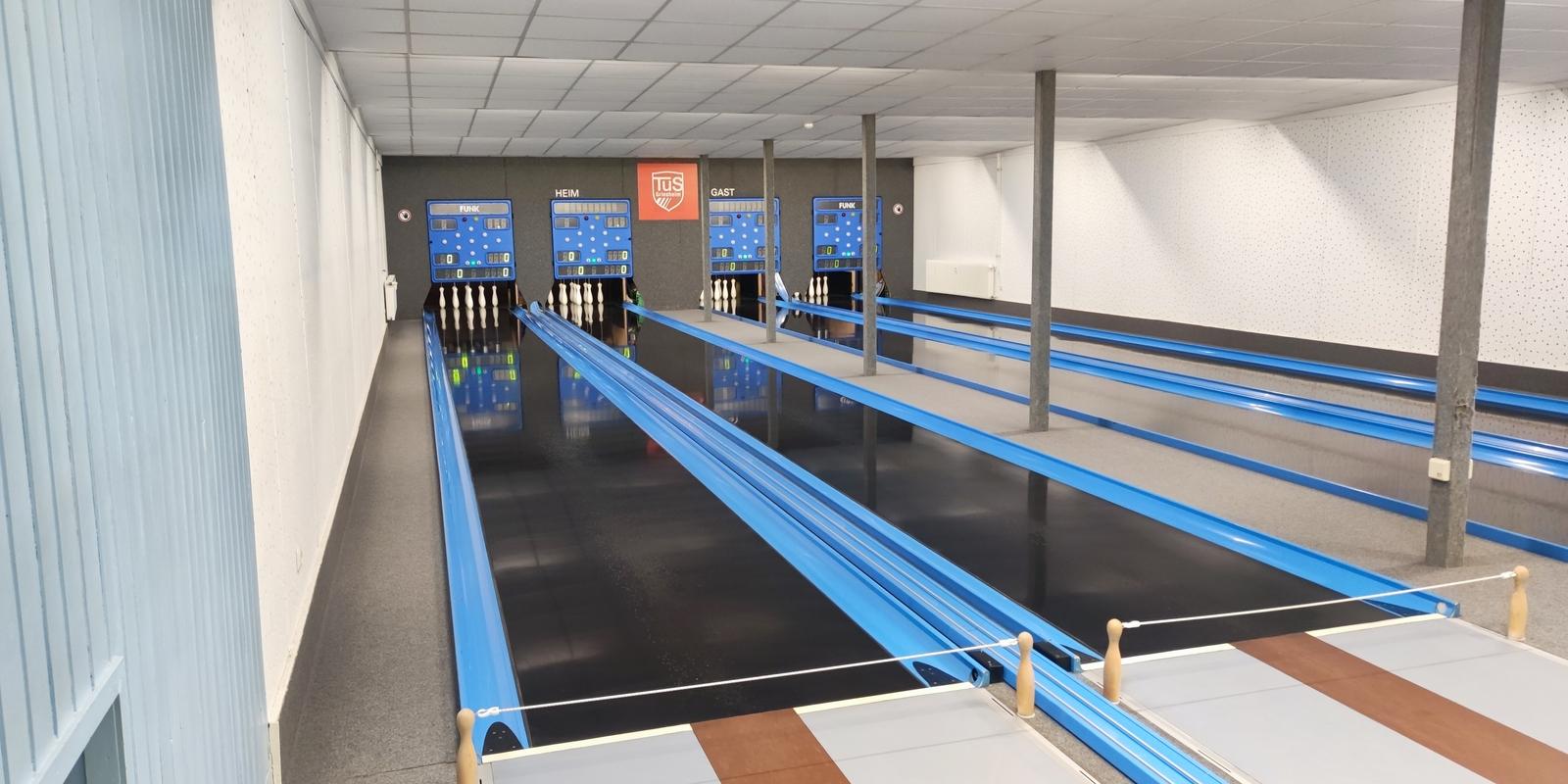 Blick auf eine moderne Kegelbahn mit blauen Bahnen, Pins und elektronischen Anzeigetafeln im Hintergrund.