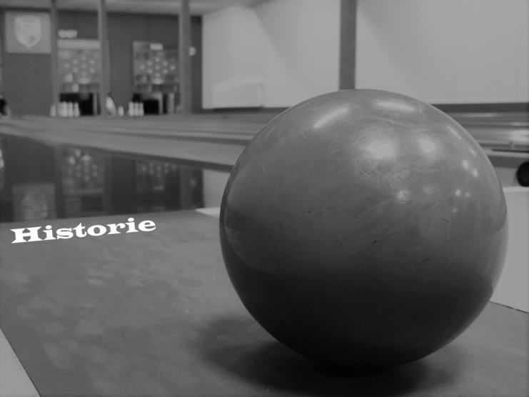 Nahaufnahme einer schwarzen Kegelbahn-Kugel auf einer Kegelbahn mit verschwommenem Hintergrund und dem Schriftzug „Historie“.