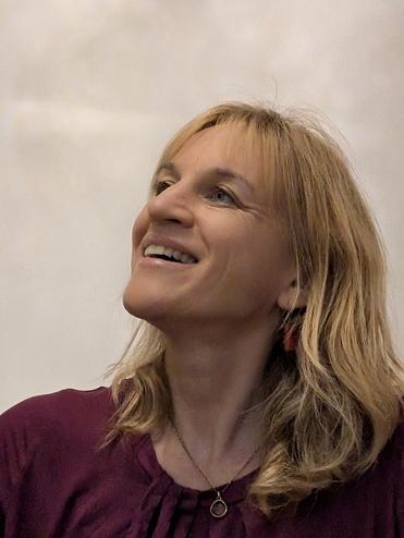 Frau mit blonden, langen Haaren lächelt und schaut nach oben, trägt ein lila Oberteil und eine goldene Kette.