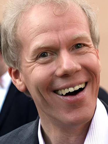 Lächelnder Mann mit kurzem, blonden Haar und hellen Augen, trägt einen schwarzen Anzug mit heller Hemdkragen.