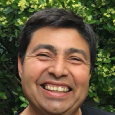 Lächelnder Mann vor grünem Hintergrund mit Pflanzen, trägt ein schwarzes T-Shirt.