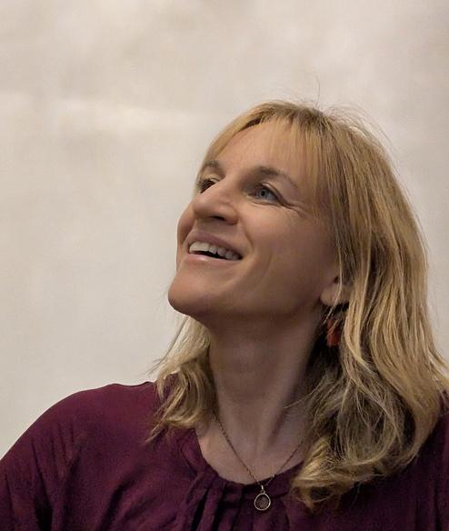 Frau mit blonden, langen Haaren lächelt und schaut nach oben, trägt ein lila Oberteil und eine goldene Kette.