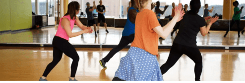 Gruppe von Tänzern in einem Spiegelsaal, die synchron zu Musik eine Choreografie vorführen.