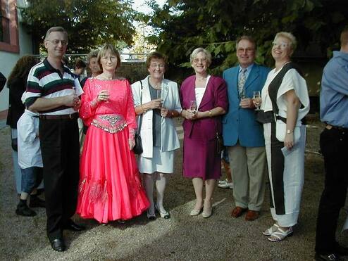Gruppe von fünf Personen in festlicher Kleidung bei einer Veranstaltung, jeder hält ein Getränk in der Hand.