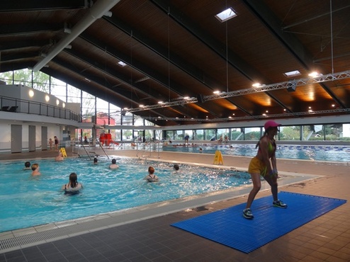 Schwimmbad mit mehreren Personen im Wasser und einer Damen in Sportkleidung auf einer Matte am Rand.