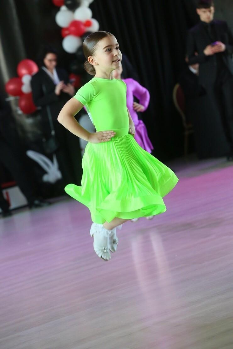 Mädchen in neongrünem Tanzkleid springt auf einer Tanzfläche mit festlichem Hintergrund.