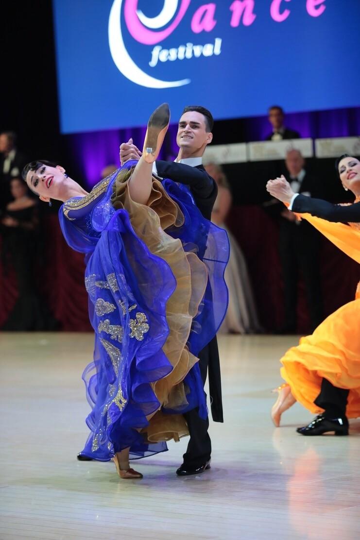 Tanzpaar in festlicher Kleidung bei einer Performance; Frau hebt ein Bein an, w&auml;hrend der Mann sie unterst&uuml;tzt.