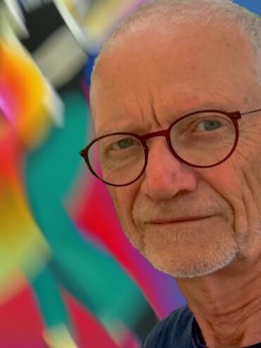 Portr&auml;t eines Mannes mit Brille vor einem bunten, unscharfen Hintergrund mit tanzenden Figuren.