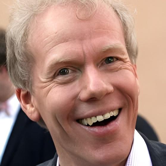 L&auml;chelnder Mann mit kurzem, blonden Haar und hellen Augen, tr&auml;gt einen schwarzen Anzug mit heller Hemdkragen.