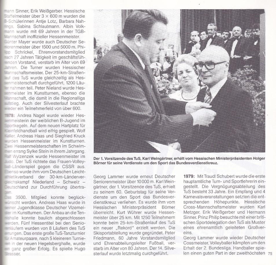 Zwei Männer, einer in Anzug und Krawatte, überreicht einem älteren Mann eine Auszeichnung. Im Hintergrund Zuschauer bei Feierlichkeit.