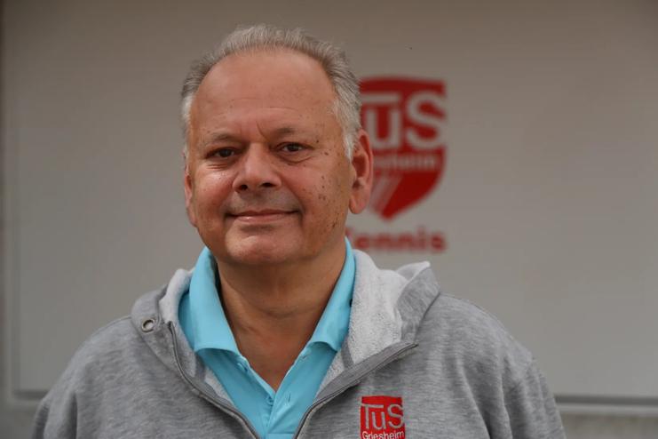 Portr&auml;t eines l&auml;chelnden Mannes in einem grauen Sweatshirt mit Logo der TuS Grafenau, vor einem neutralen Hintergrund.