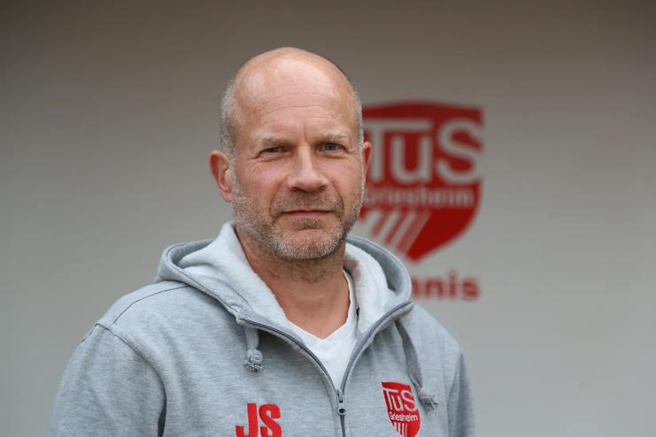 Portr&auml;t eines Mannes mit Glatze in Sportjacke, Hintergrund mit dem Logo des TuS Tischtennisvereins.