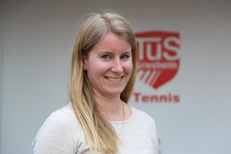 Portr&auml;t einer l&auml;chelnden Frau mit langen blonden Haaren vor einer Wand mit dem Logo eines Tischtennisvereins.