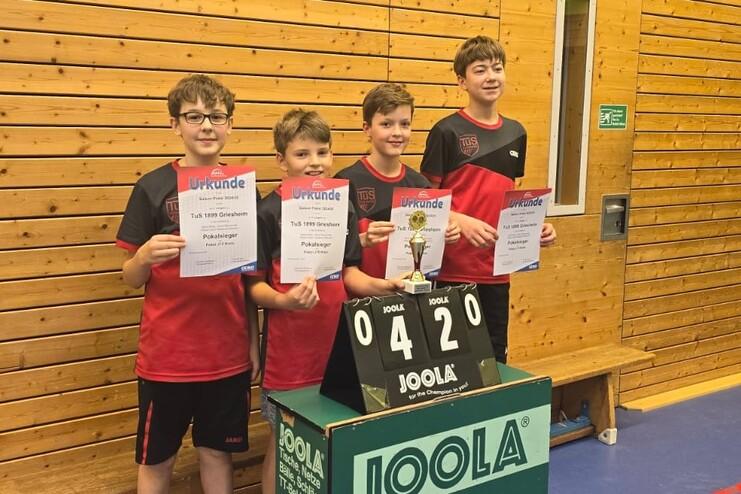 Vier Jugendliche in roten Sporttrikots halten Urkunden und einen Pokal auf einem Tischtennisturnier.