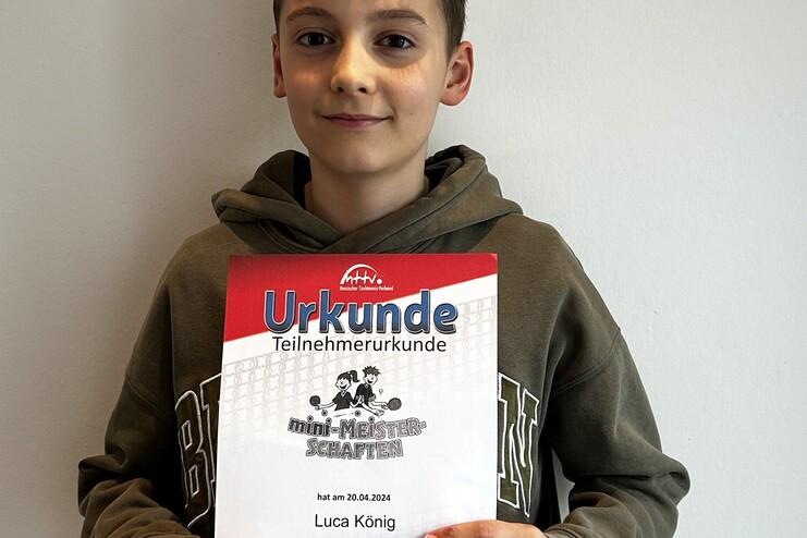 Junger Junge hält stolz eine Teilnahmeurkunde für die mini-Meisterschaften in der Hand.