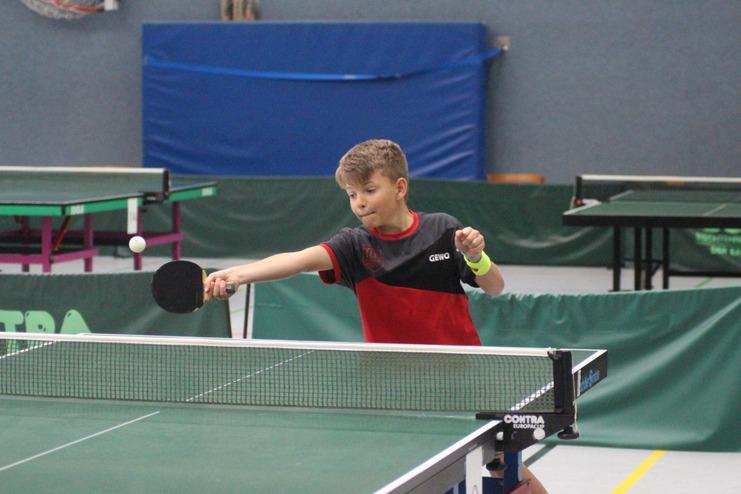 Ein Junge schlägt einen Tischtennisball mit einem Schläger über das Netz auf einer grünen Tischtennisplatte.