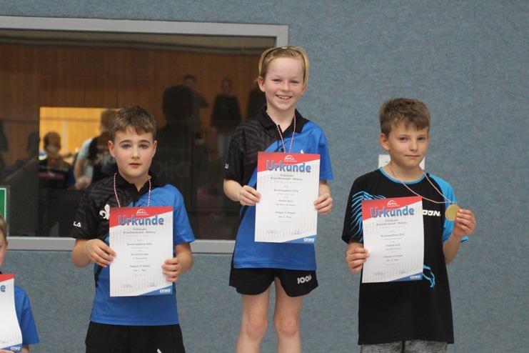 Drei Kinder stehen mit Urkunden auf einem Siegertreppchen nach einem Tischtennisturnier.