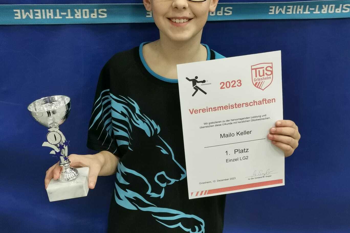 Junger Sportler hält Pokal und Urkunde für den ersten Platz bei den Vereinsmeisterschaften in der Hand.