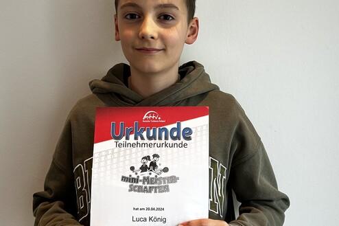 Junger Junge hält stolz eine Teilnahmeurkunde für die mini-Meisterschaften in der Hand.