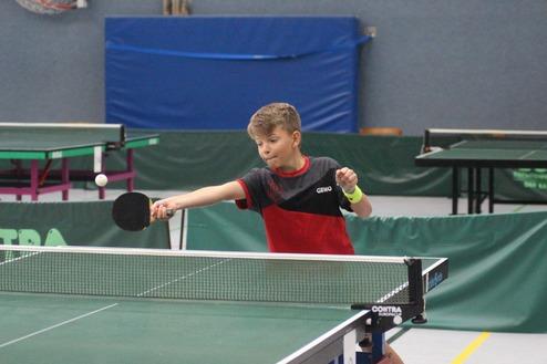 Ein Junge schlägt einen Tischtennisball mit einem Schläger über das Netz auf einer grünen Tischtennisplatte.
