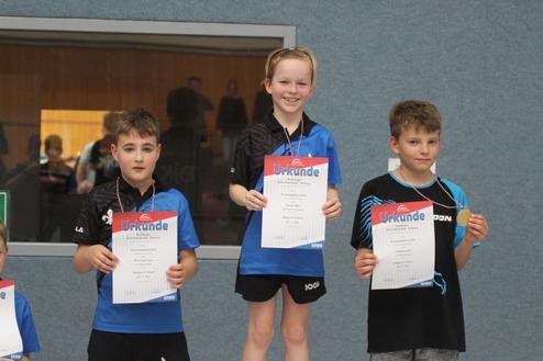 Drei Kinder stehen mit Urkunden auf einem Siegertreppchen nach einem Tischtennisturnier.